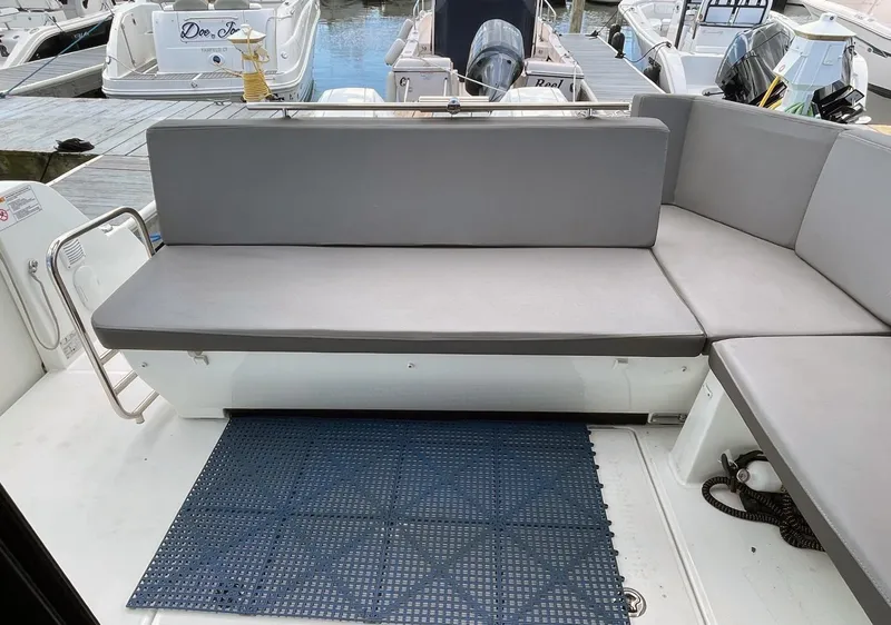 Slide: The Image of 2023 Beneteau Antares 11 OB boat seating area with gray cushions and docked boats in background. - 4
