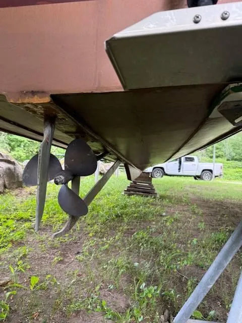 Slide: The Image of 1968 Lyman 19 boat underside with propeller, parked on grass near a truck. - 19