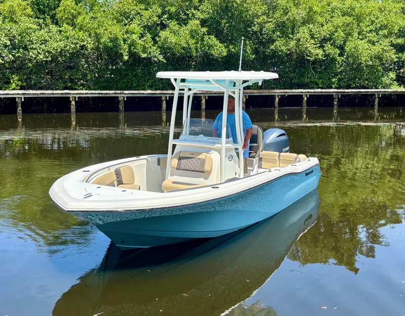 Slide: The Image of 2022 Tidewater 210 LXF boat on calm water, surrounded by lush greenery. - 1