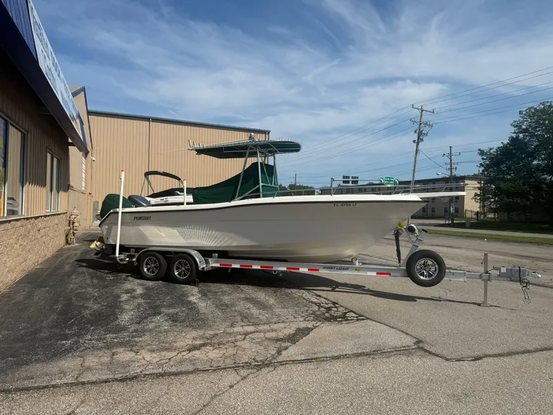 Slide: The Image of 2002 Pursuit 2470 CC boat on trailer, parked outside a building under a clear sky. - 21