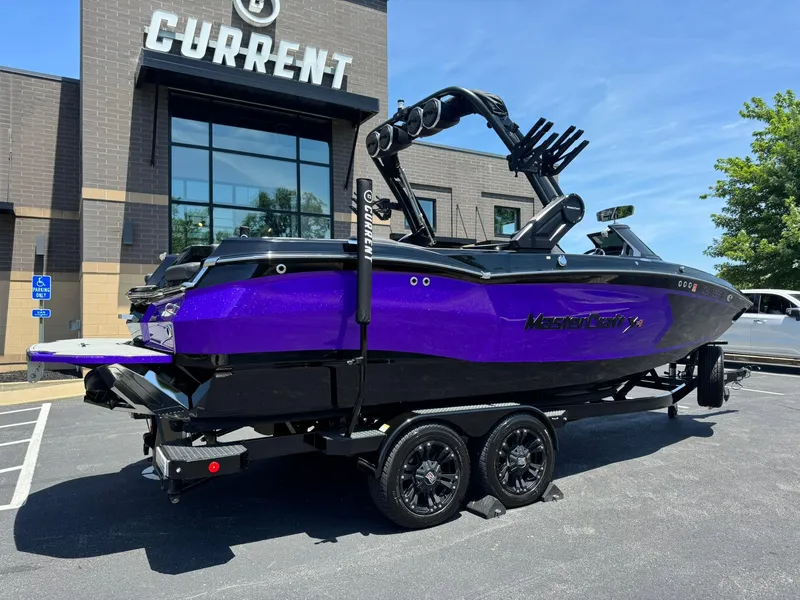 Slide: The Image of 2023 MasterCraft XStar S Piranha boat in vibrant purple, parked outside a building. - 2