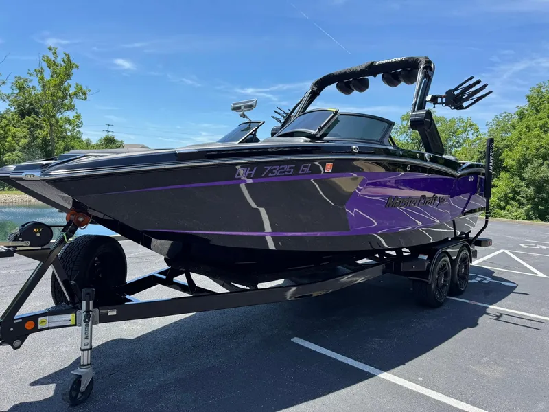 Slide: The Image of 2023 MasterCraft XStar S Piranha boat on trailer, black and purple design, parked outdoors. - 23
