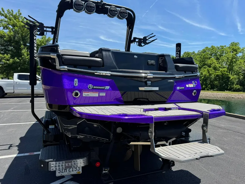 Slide: The Image of 2023 MasterCraft XStar S Piranha boat, vibrant purple, parked near a lake. - 25