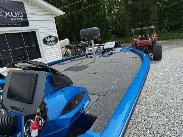 Slide: The Image of 2026 Vexus 2085s boat in blue, parked outside dealership with tractor nearby. - 6