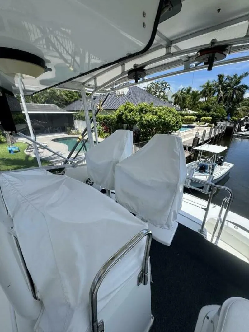 Slide: The Image of 1989 Hatteras 42 Convertible yacht deck with covered seats, docked near a waterfront property. - 18