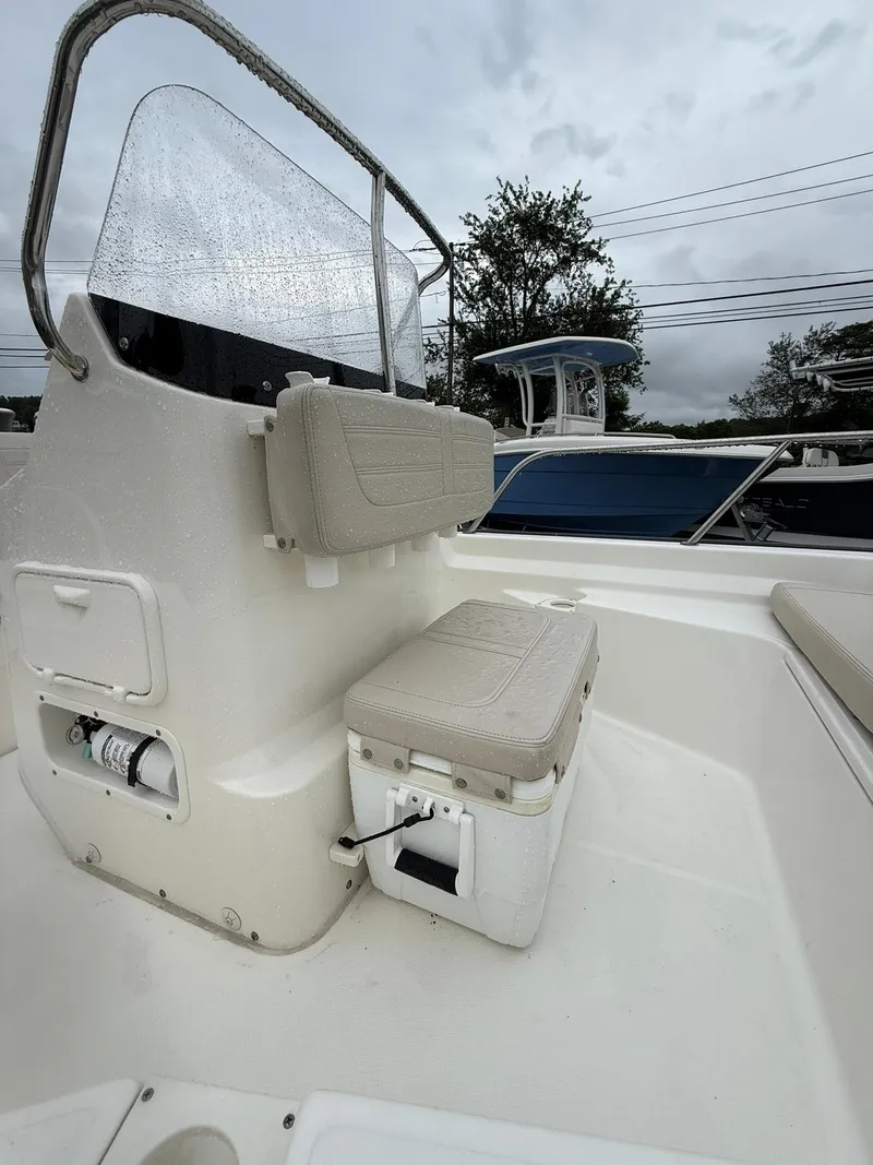 Slide: The Image of 2019 Boston Whaler 150 Montauk interior with seating and storage, under cloudy skies. - 5