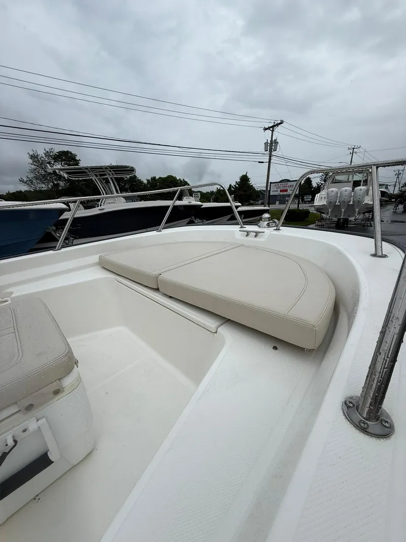 Slide: The Image of 2019 Boston Whaler 150 Montauk boat interior with cushioned seating, overcast sky background. - 6