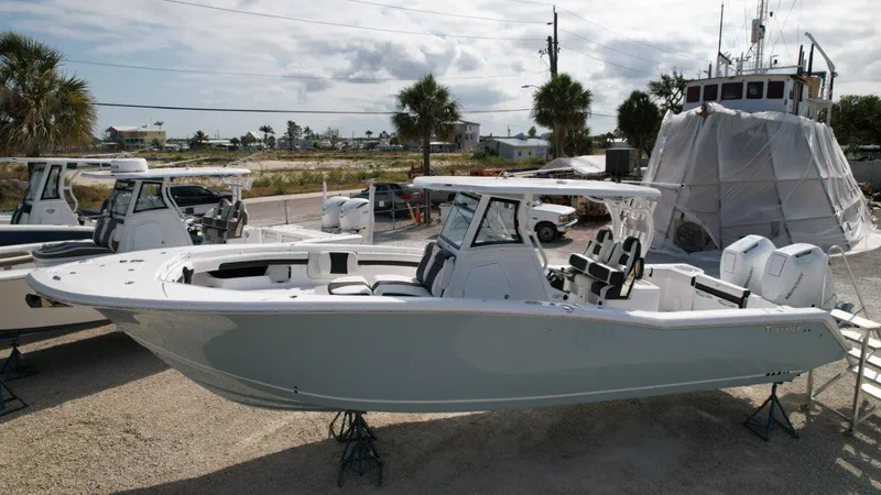 Slide: The Image of 2025 Tidewater 320 CC Adventure boat on stands, under a cloudy sky. - 2