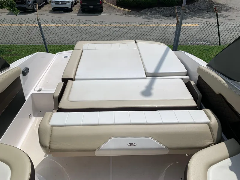 Slide: The Image of 2014 Regal 27 FasDeck boat interior with beige and white seating, parked near a fence. - 14