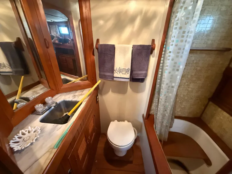 Slide: The Image of 1981 DeFever Passagemaker bathroom with sink, toilet, and shower, featuring wooden cabinetry. - 23