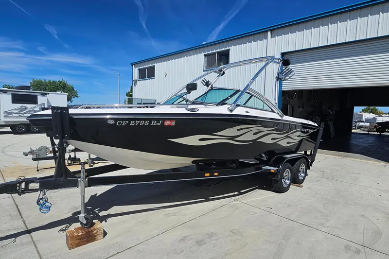 The Image of 2007 Supreme V232 boat on trailer, parked outside a garage under clear blue sky. - 20