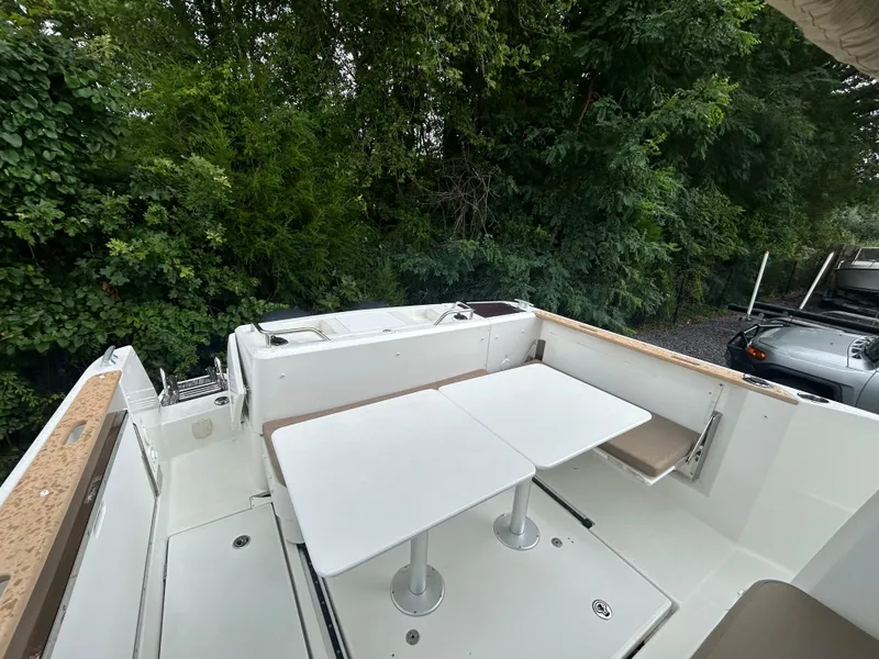 Slide: The Image of 2015 Jeanneau Merry Fisher 855 Marlin deck with seating and table, surrounded by greenery. - 3