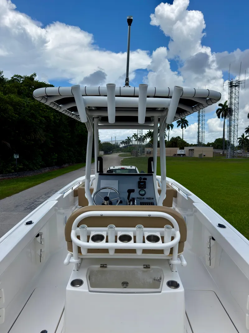 Slide: The Image of 2023 Bayliner Trophy T24CC boat with T-top and rod holders, parked on a grassy area. - 23