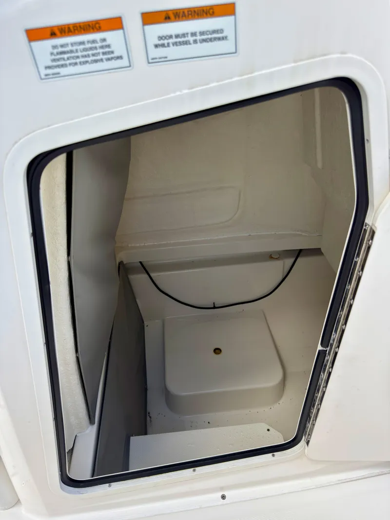 Slide: The Image of 2023 Bayliner Trophy T24CC storage compartment with warning labels, open door view. - 25