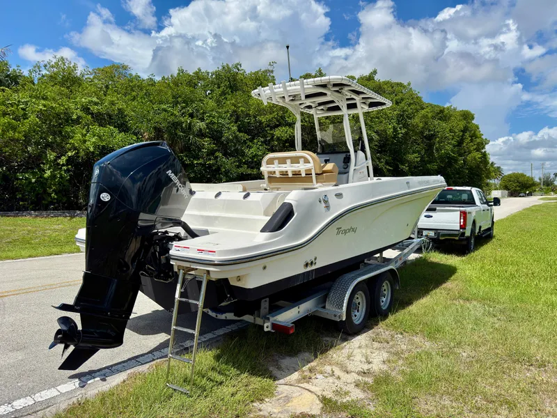 Slide: The Image of 2023 Bayliner Trophy T24CC boat on trailer, parked beside a road with lush greenery. - 4