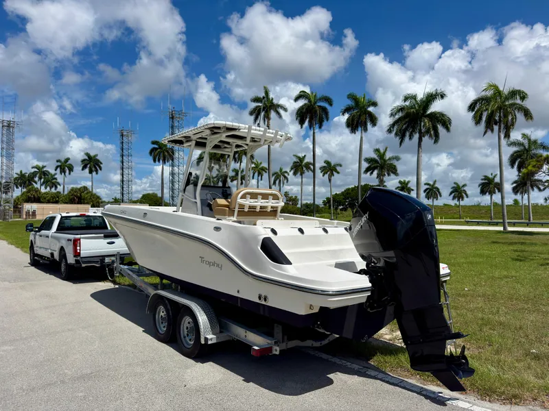 Slide: The Image of 2023 Bayliner Trophy T24CC boat on trailer, parked near palm trees under blue sky. - 6