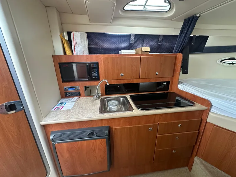 Slide: The Image of 2008 Bayliner 300SB boat interior with kitchenette, featuring sink, microwave, and storage cabinets. - 16