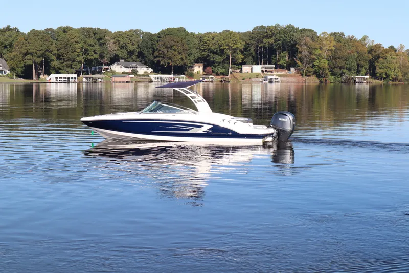 The Image of 2024 Chaparral 23 SSi OB boat cruising on a serene lake with wooded shoreline. - 0