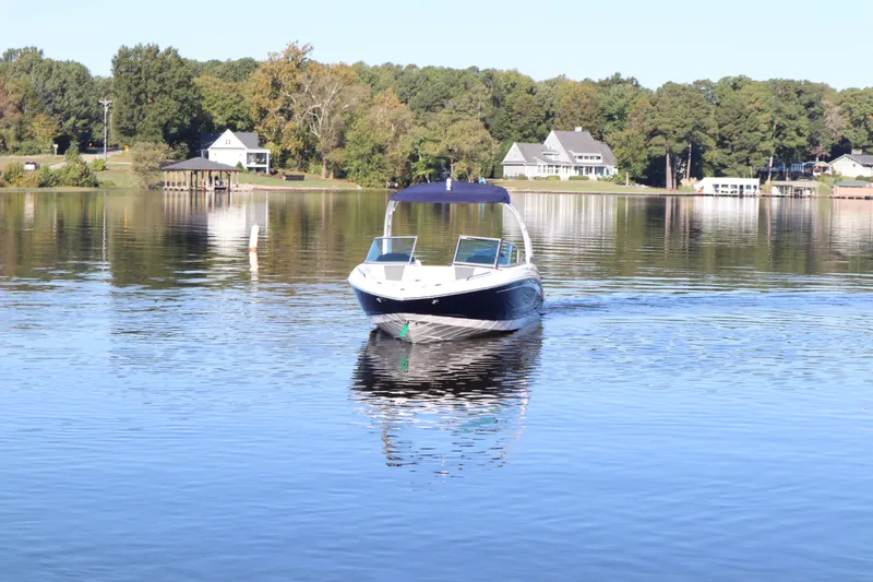 Slide: The Image of 2024 Chaparral 23 SSi OB boat cruising on a serene lake with houses in the background. - 2