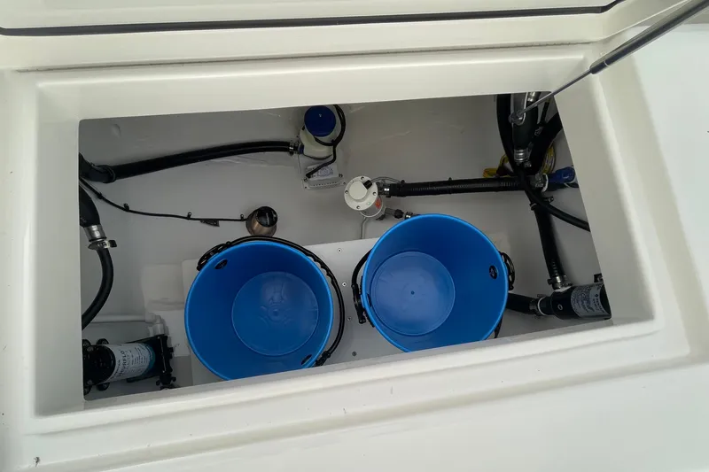 Slide: The Image of 2026 Regulator 25 boat storage compartment with blue buckets and plumbing components. - 25