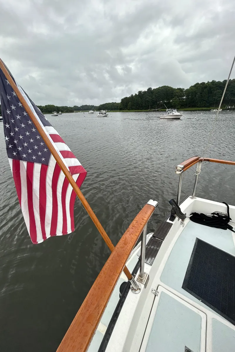 Slide: The Image of American flag on a 1998 Monk 36 boat, cruising on a calm river. - 22