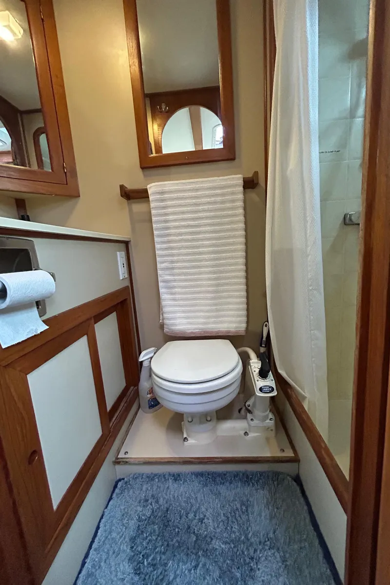 Slide: The Image of Compact bathroom in a 1998 Monk 36 boat, featuring a toilet, shower, and wooden cabinetry. - 5