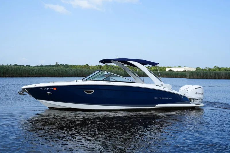 Slide: The Image of 2023 Regal 29 OBX boat on calm water with lush greenery background. - 7