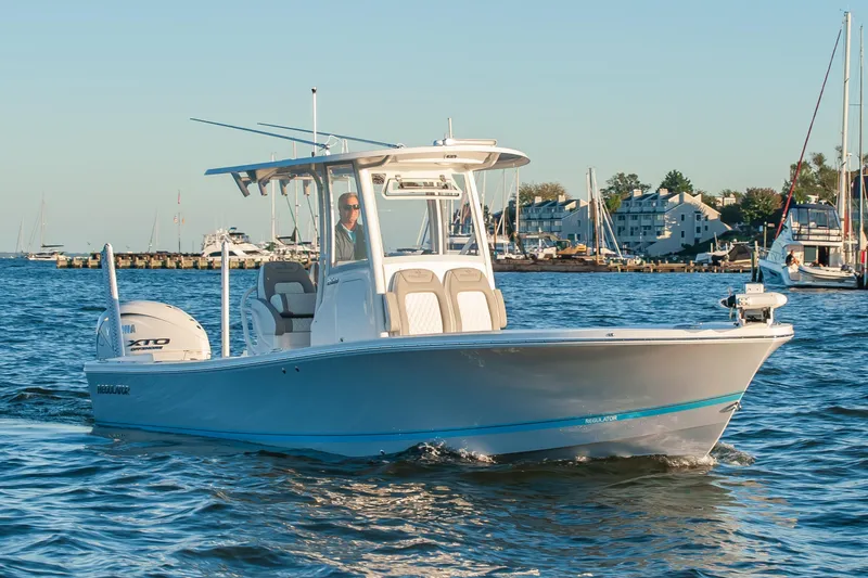 Slide: The Image of 2026 Regulator 26XO boat cruising on calm waters near a marina. - 2