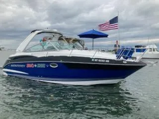 Slide: The Image of 2019 Monterey 295 Sport Yacht on water with American flag, cloudy sky. - 2