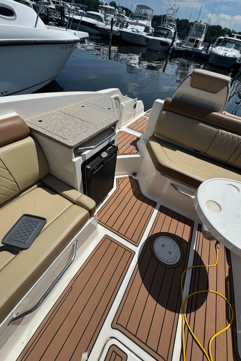 Slide: The Image of 2015 Sea Ray 290 Sundeck interior with tan seating and wood flooring at a marina. - 20