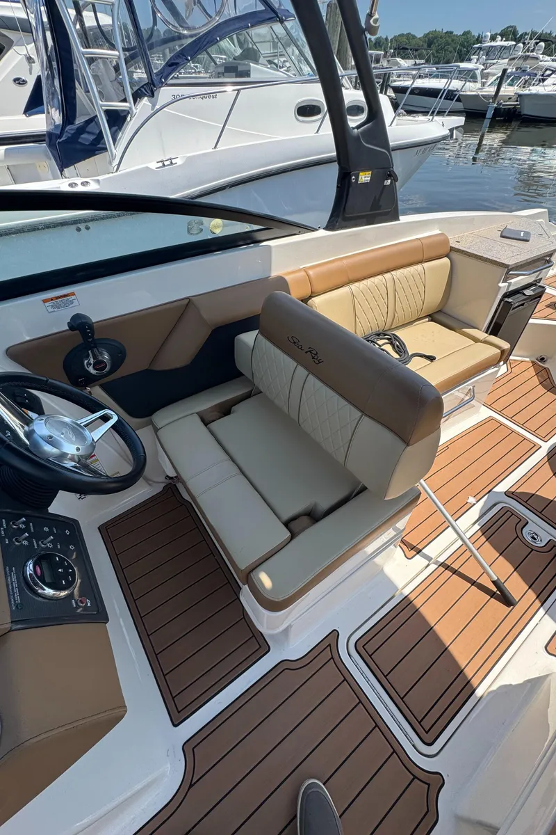Slide: The Image of 2015 Sea Ray 290 Sundeck interior with tan seating and wood accents at marina. - 26