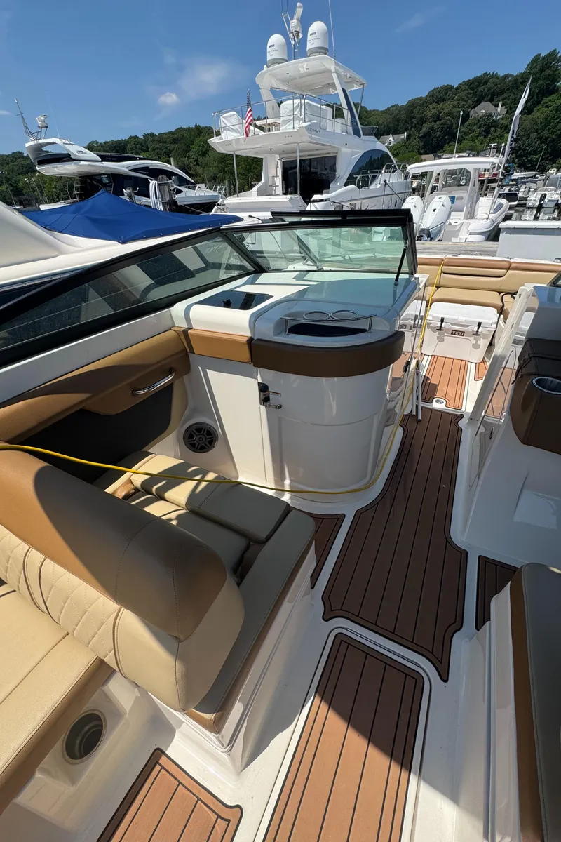 Slide: The Image of 2015 Sea Ray 290 Sundeck interior with tan seating and wood-style flooring at a marina. - 7