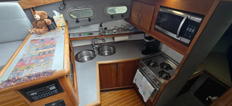 Slide: The Image of 1991 Bayliner 3288 Motoryacht kitchen with dual sinks, stove, microwave, and wooden cabinetry. - 24