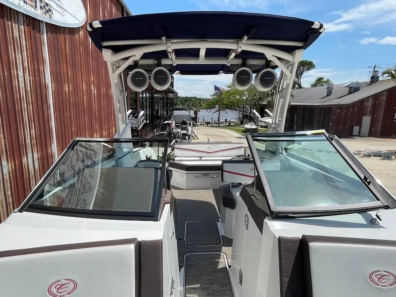 Slide: The Image of 2023 Cobalt R8 Surf boat with open deck and speakers, docked near a rustic building. - 14