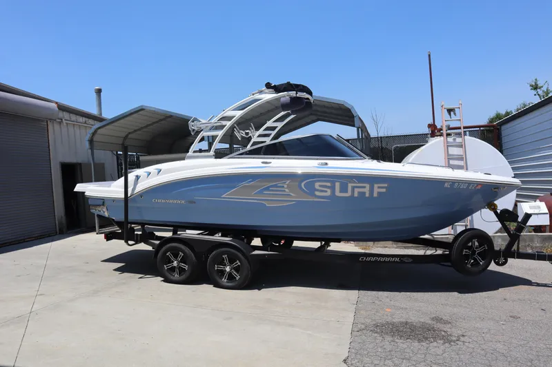 The Image of 2023 Chaparral 23 Surf boat on trailer, parked outdoors under a metal canopy. - 0