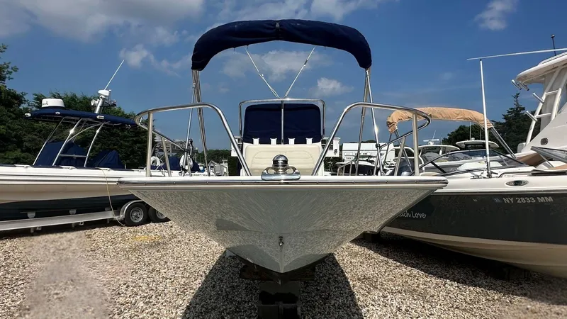 Slide: The Image of 2022 Boston Whaler 150 Montauk boat with blue canopy, parked on gravel, surrounded by other boats. - 23