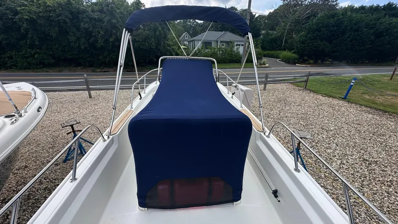 Slide: The Image of 2022 Boston Whaler 150 Montauk boat with blue cover, parked on gravel. - 7