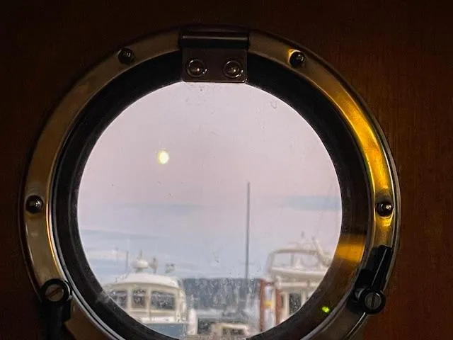 Slide: The Image of Porthole view from 1974 Willard Nomad, showcasing boats and a serene sunset. - 33
