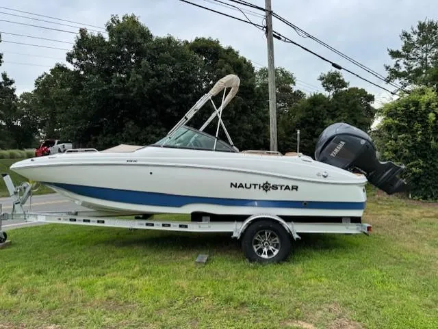 The Image of 2025 NauticStar 203 DC Deck boat on trailer, parked on grass. - 12