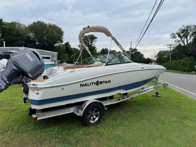 Slide: The Image of 2025 NauticStar 203 DC Deck boat on trailer, parked on grass beside a road. - 14
