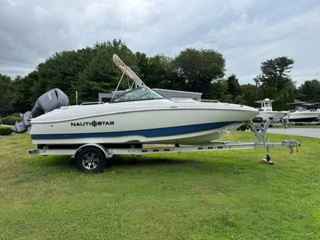 Slide: The Image of 2025 NauticStar 203 DC Deck boat on trailer, parked on grass with trees in background. - 16
