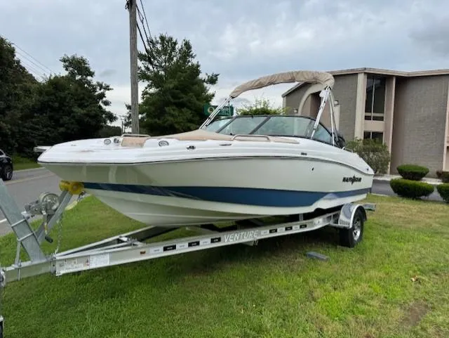Slide: The Image of 2025 NauticStar 203 DC Deck boat on trailer, parked on grass near building. - 17