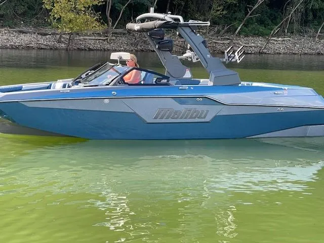 Slide: The Image of 2023 Malibu M240 boat on calm green water, with trees in the background. - 1