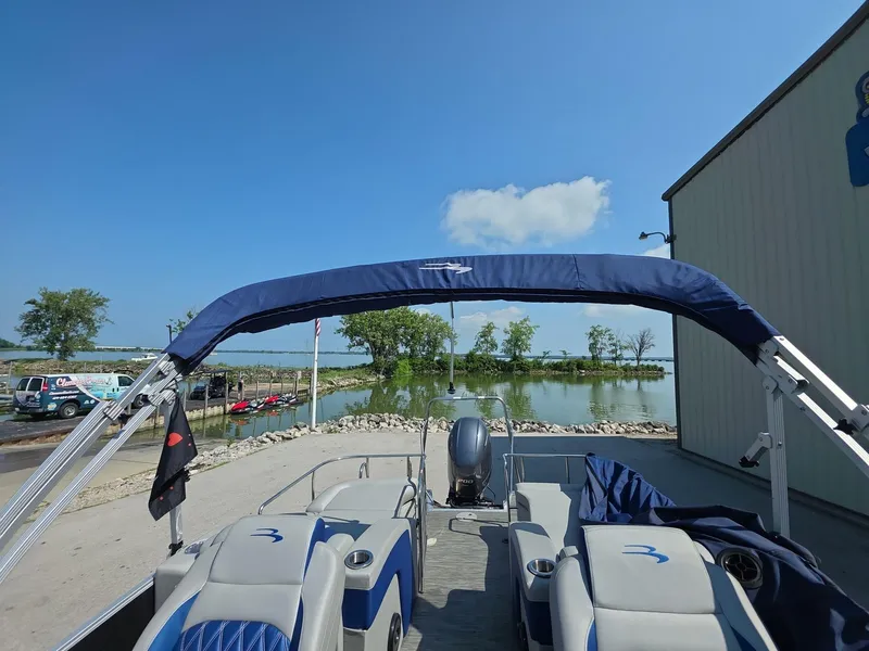Slide: The Image of 2021 Bennington Q 23 Swingback pontoon boat with blue cover, parked near a lake. - 10