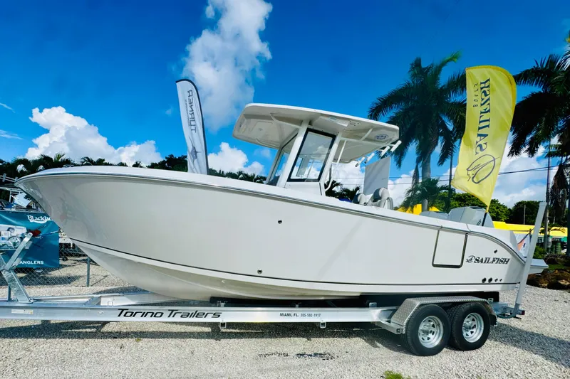 The Image of 2026 Sailfish 252 CC boat on trailer, displayed outdoors with flags and palm trees. - 2
