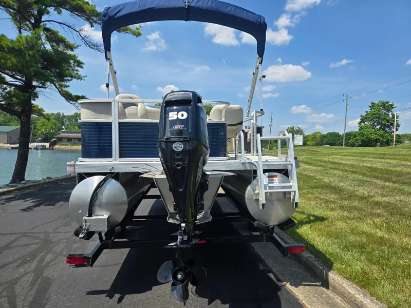 Slide: The Image of 2019 Bennington 188 SFV pontoon boat with 50 HP motor, docked near a grassy area. - 2