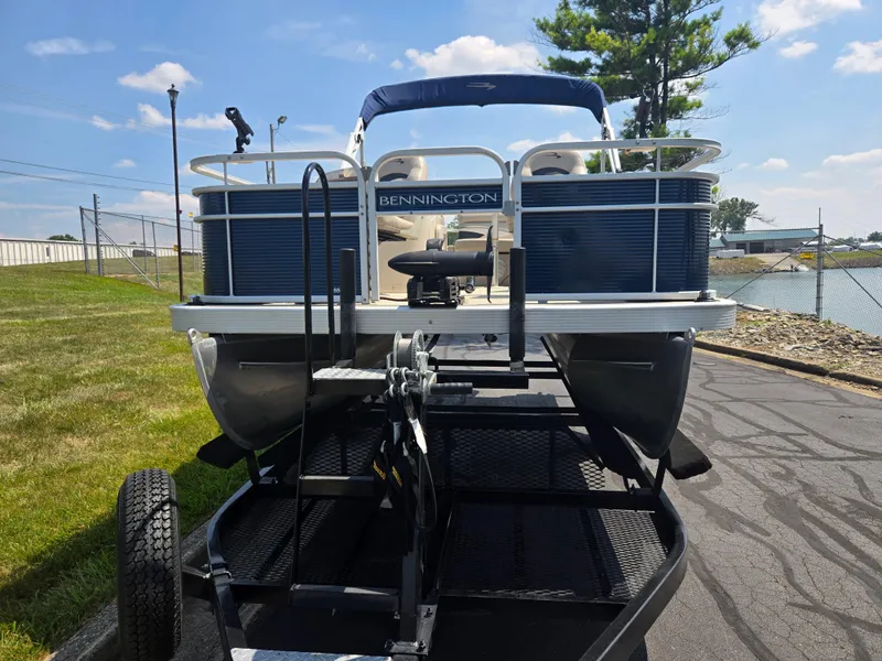 Slide: The Image of 2019 Bennington 188 SFV pontoon boat on trailer, parked near a lake under a clear sky. - 6