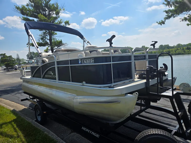 Slide: The Image of 2019 Bennington 188 SFV pontoon boat on trailer by a lake under a clear sky. - 8