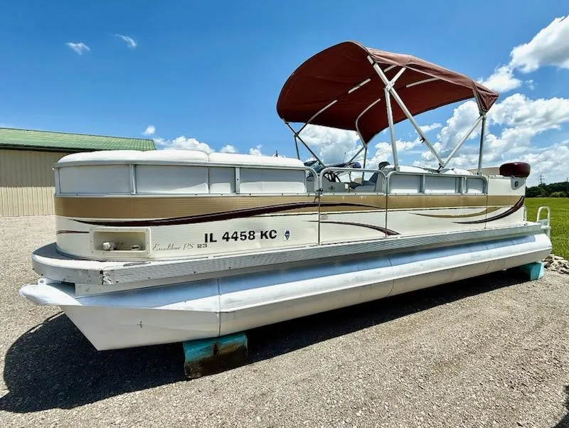 The Image of 2005 Avalon EXCALIBER 2325 pontoon boat with canopy, parked on gravel under blue sky. - 1