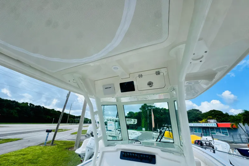 Slide: The Image of 2026 Sailfish 272 CC boat interior with console and overhead storage, parked near a boating center. - 15